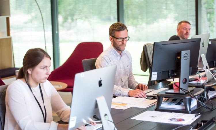 Two men and one woman in office space on computers